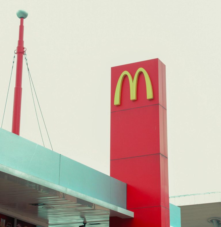 A McDonald's signage on a red pillar against an overcast sky showcases its iconic logo at an urban location.